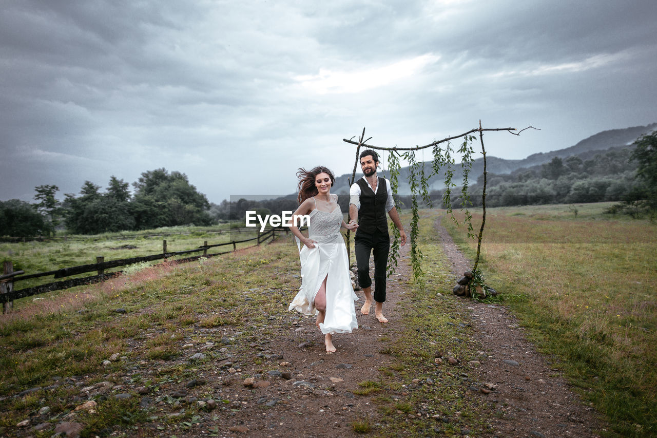 Beautiful woman holding hands of man while running on grassy field