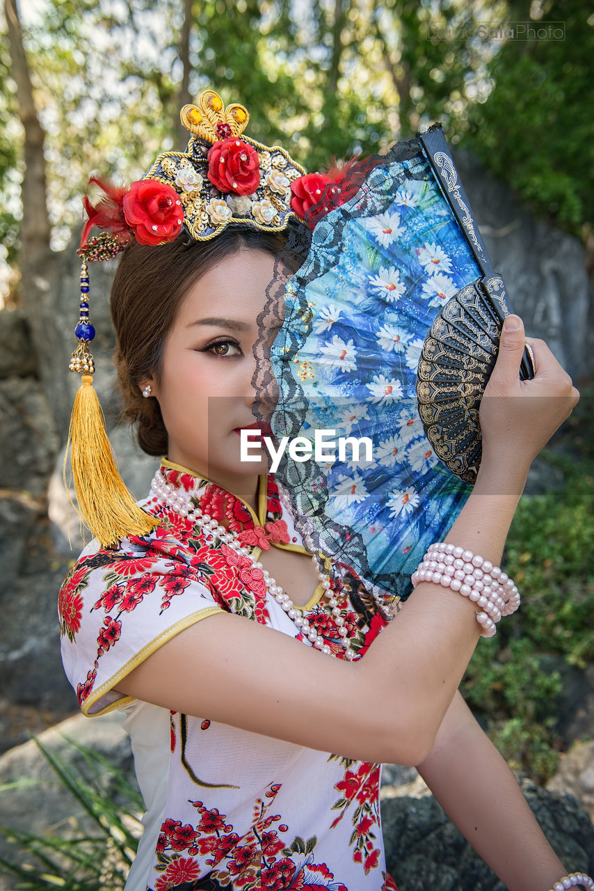 Portrait of young woman wearing qipao holding hand fan