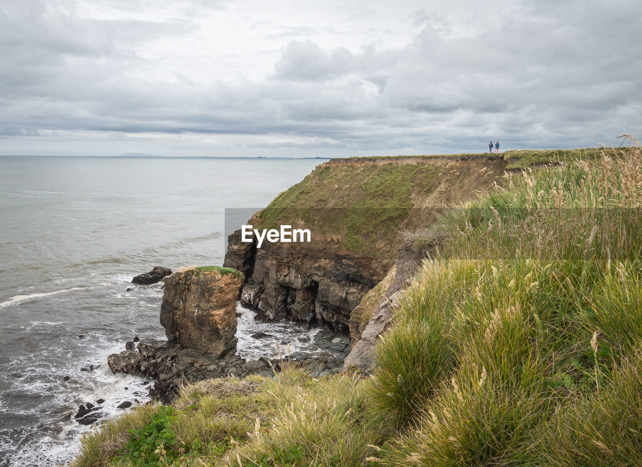 Couple standing on the edge of cliff enjoying view on ocean, southland region of new zealand