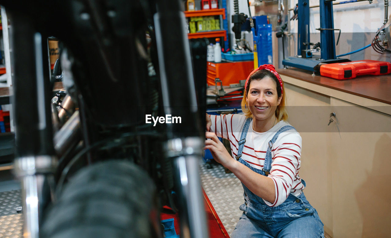 Portrait of mechanic woman repairing motorcycle on factory