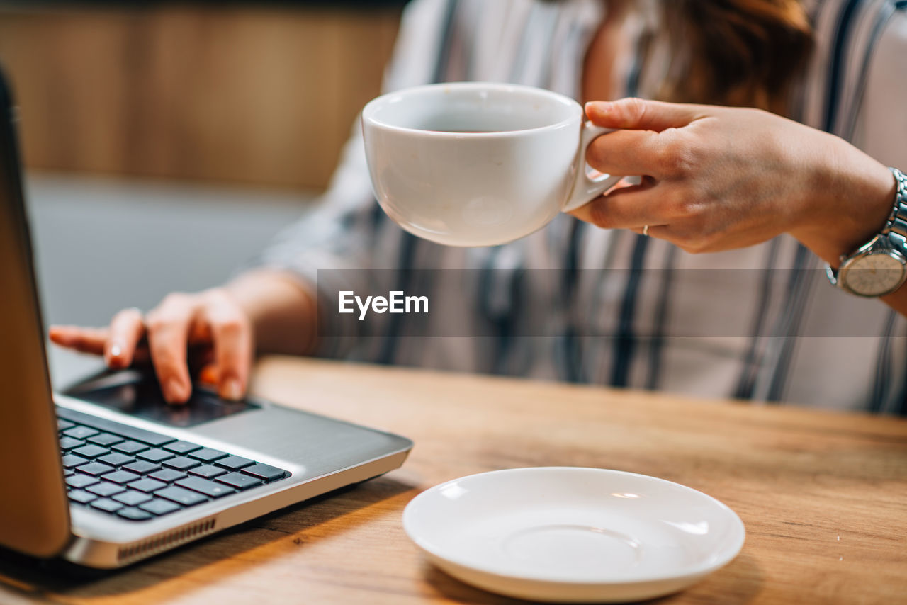 Midsection of businesswoman having coffee while using laptop in office