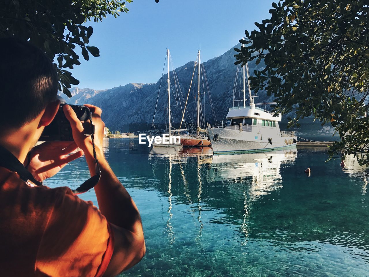 Cropped image of man photographing boats moored at harbor