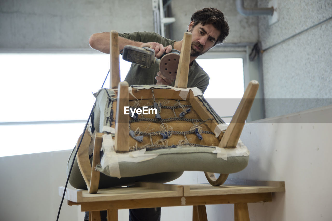 Low angle view of a man repairing and restoring an old chair