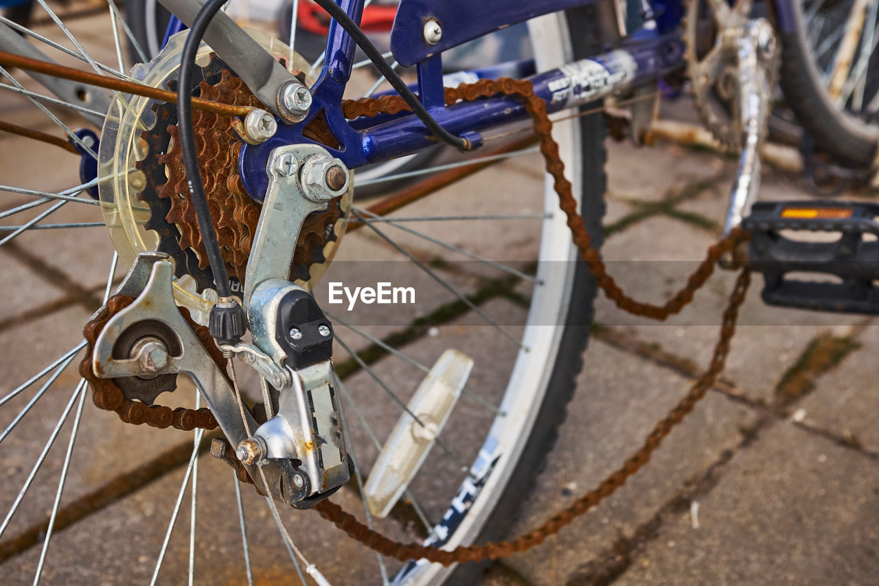 Blue bike has been outside all winter and got broken. rusty bicycle chain hangs on sprocket and gear