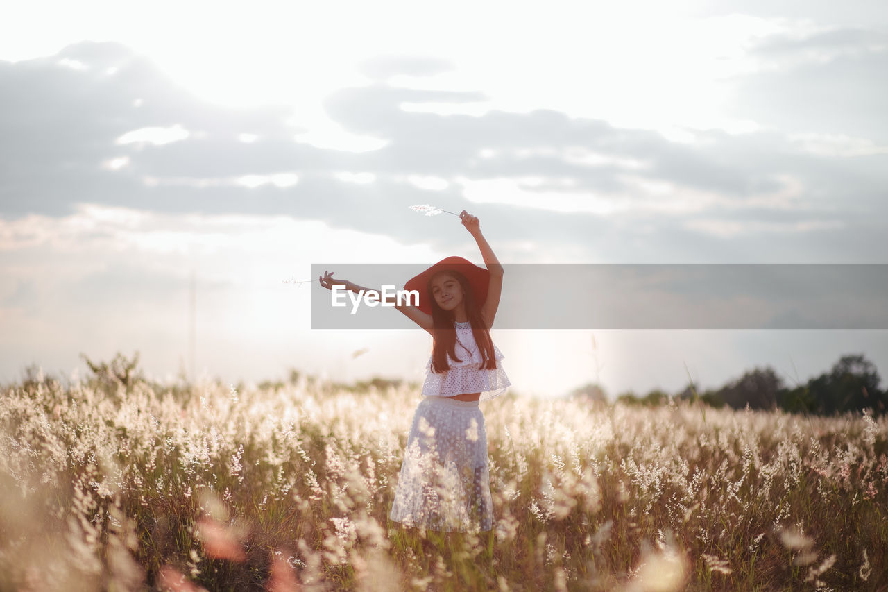 Portrait cute girl with arms raised standing amidst plants on field against sky