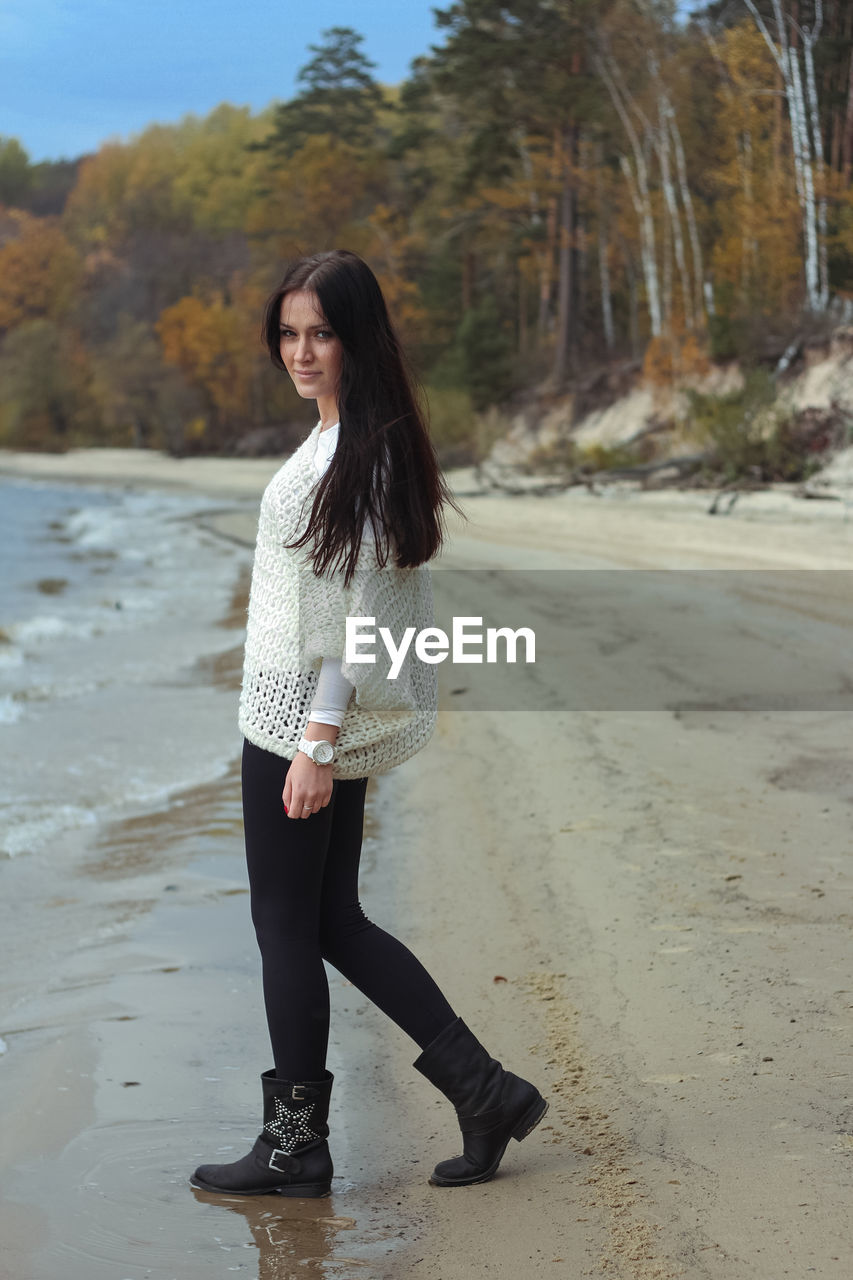 Beautiful young woman walking along the seashore in autumn