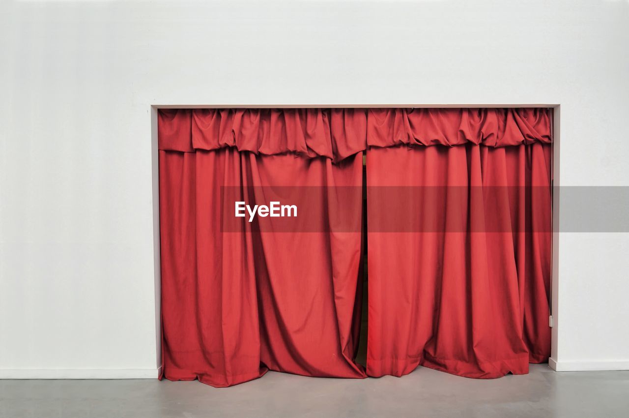 RED UMBRELLA AGAINST WALL COVERED WITH CLOSED CURTAIN