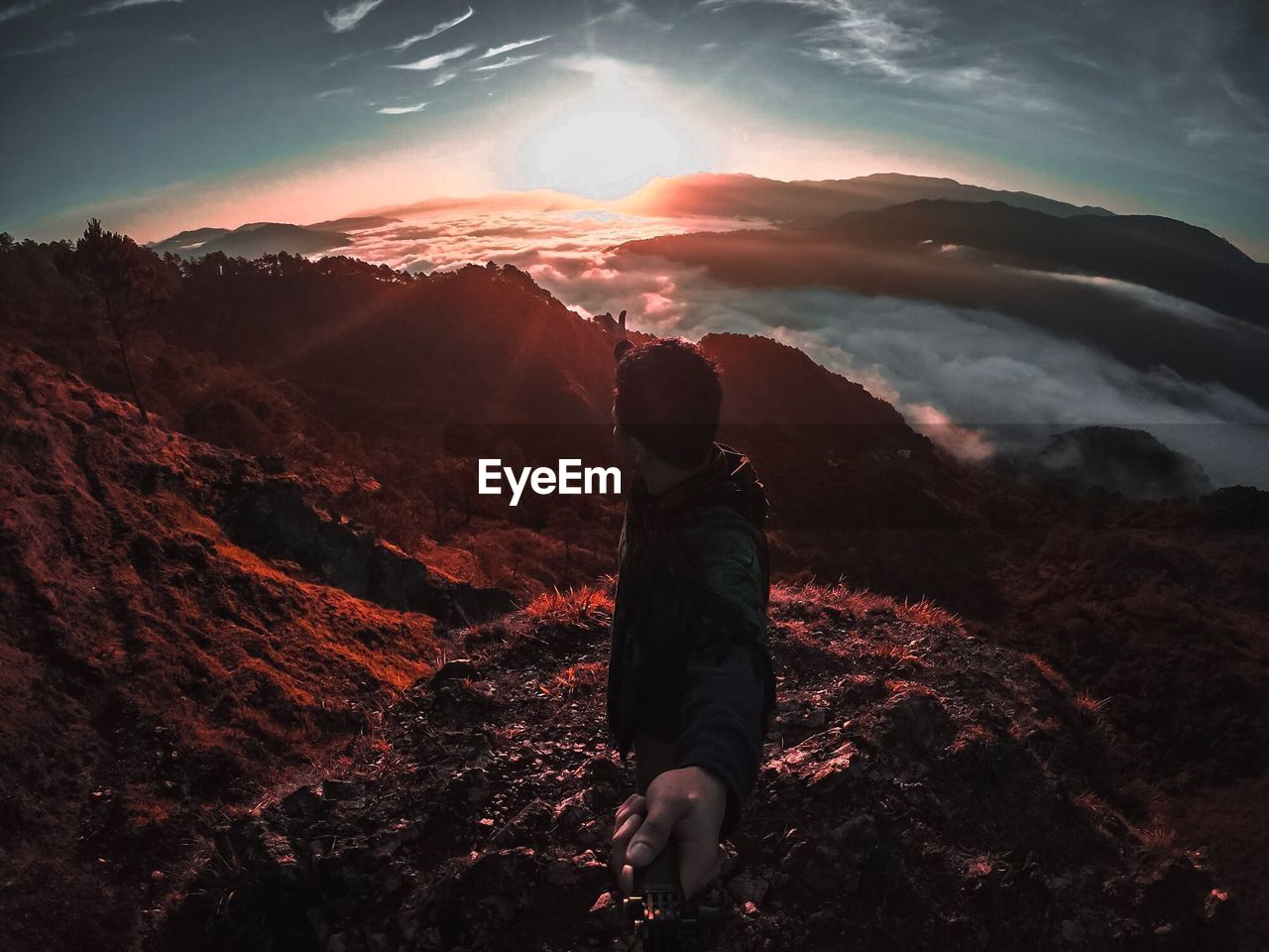 Fish-eye lens view of man standing on mountains against sky during sunset