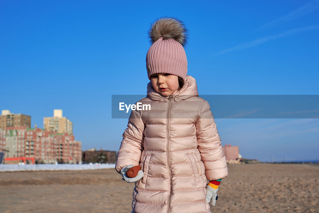 Young girl playing on the beach in winter dressed in a warm coat