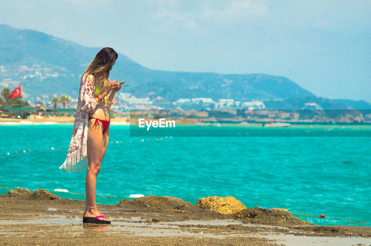 Woman standing at beach by sea against sky