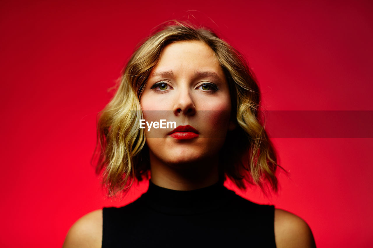 Portrait of young woman wearing lipstick against red background