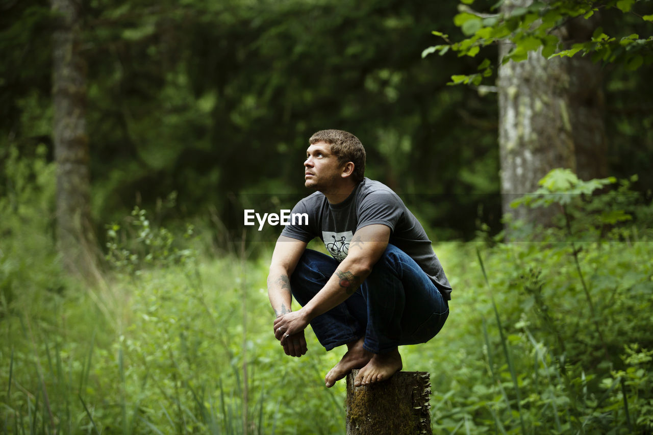 Thoughtful man crouching on wood in forest