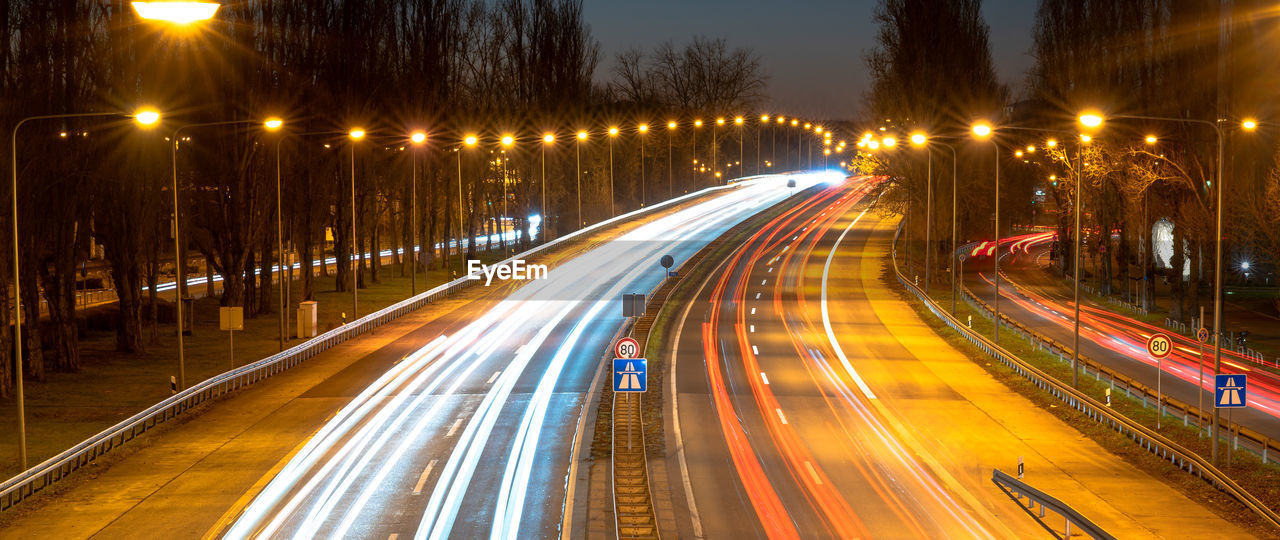 illuminated, night, transportation, light trail, motion, city, long exposure, street, speed, architecture, road, traffic, street light, blurred motion, highway, city life, mode of transportation, tail light, built structure, city street, lighting equipment, building exterior, no people, motor vehicle, light, evening, car, nature, sky, headlight, travel, lane, outdoors, infrastructure, travel destinations, on the move, light - natural phenomenon, multiple lane highway, the way forward, cityscape, dusk, vehicle light, high angle view, tree, metropolitan area, glowing