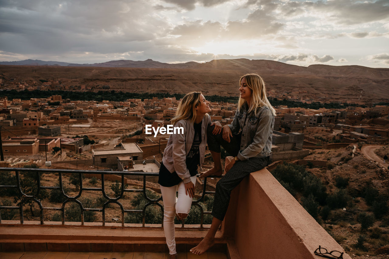 Smiling friends spending leisure time on building terrace against sky