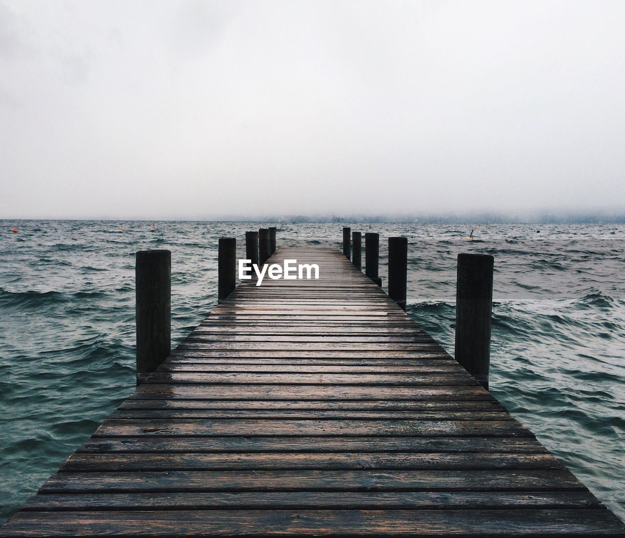 Empty jetty leading to calm sea against clear sky