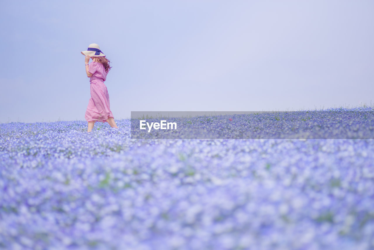 Surface level shot of woman standing amidst purple flowers on field against sky