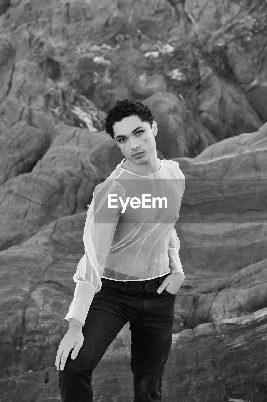 Young male with  androgynous look shot outdoor in black and white with rocks in background.