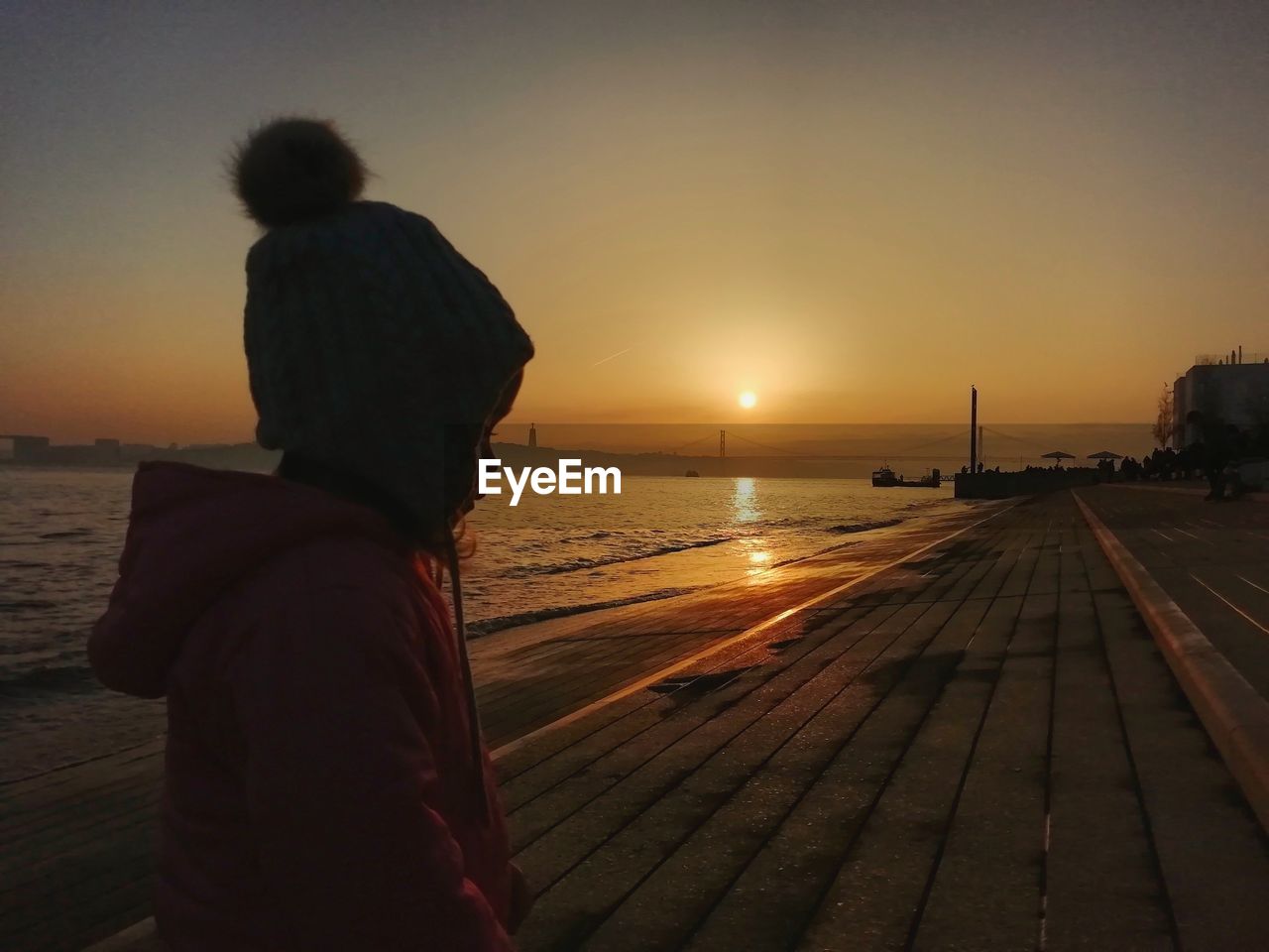 Cute girl looking away while standing at beach during sunset