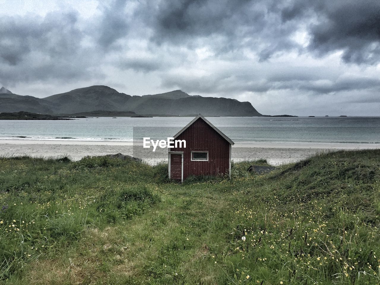 Hut on beach by mountains against cloudy sky