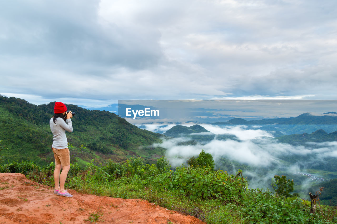 Woman photographing while standing on mountain against sky