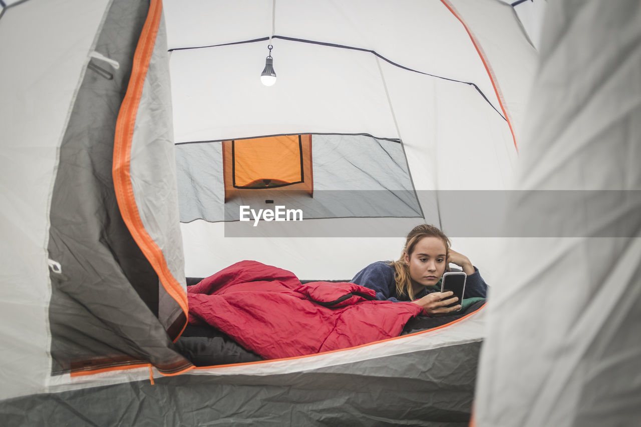 Teenage girl using smart phone while lying in tent