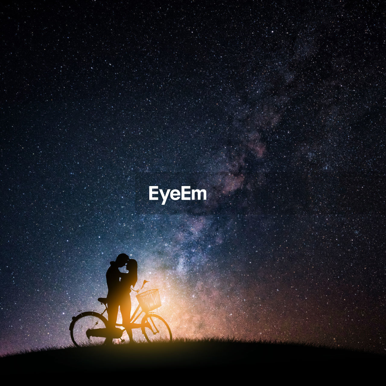 Silhouette couple romancing by bicycle against star field at night