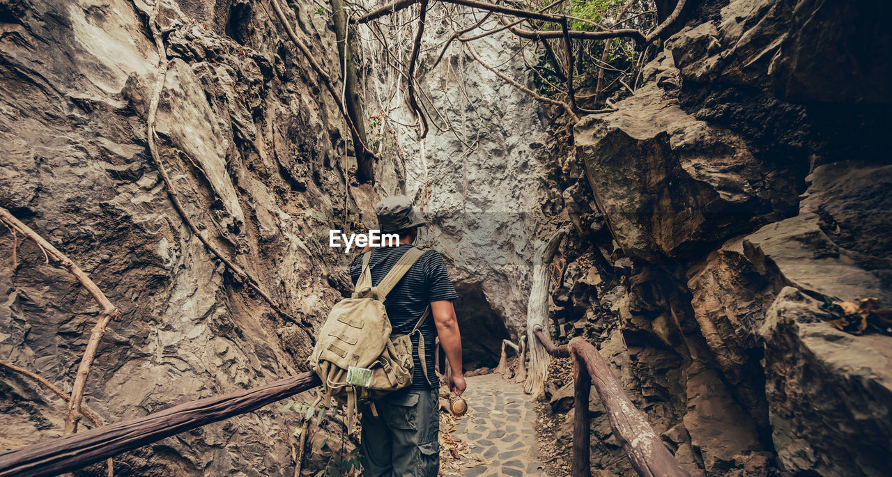 REAR VIEW OF MAN STANDING ON ROCK AT FOREST