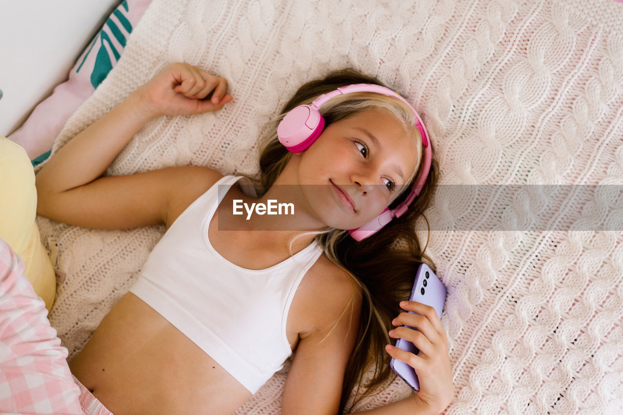 Pretty caucasian girl holds a smartphone in her hand and listens to music in wireless pink headphone