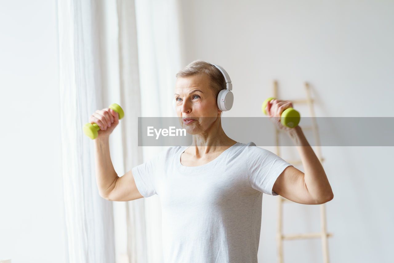 Portrait of senior woman exercising fitness with dumbbells at home. mature female build up biceps