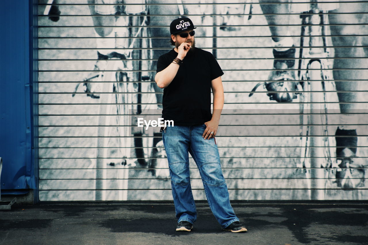 Man smoking while standing graffiti on wall