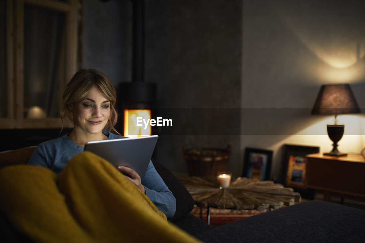 Portrait of smiling woman with tablet relaxing on couch in the evening