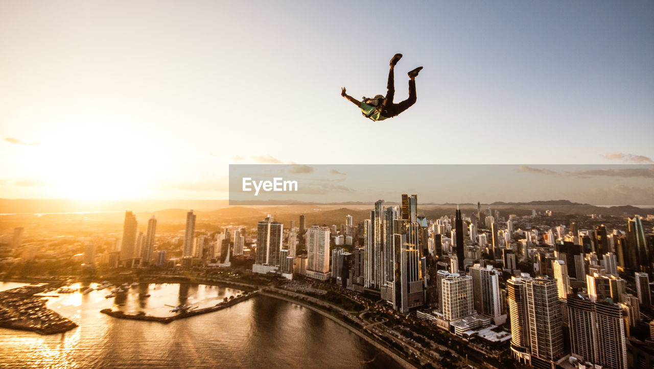 Man paragliding in mid-air in city at sunset