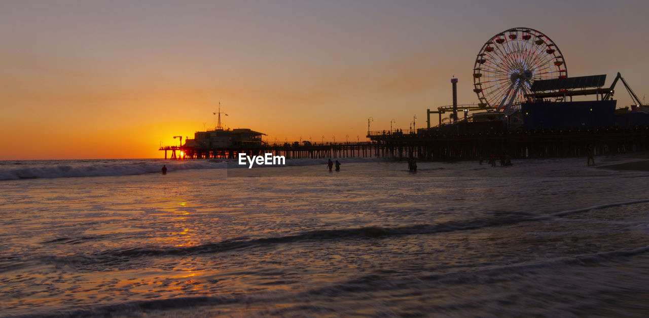 Ferris wheel at beach against sky during sunset