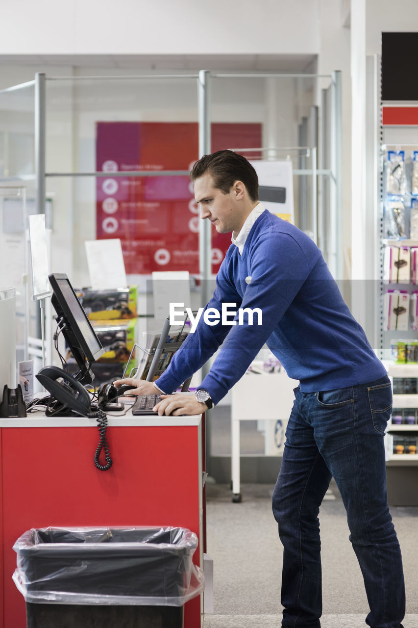 Salesman using computer while leaning on counter in store