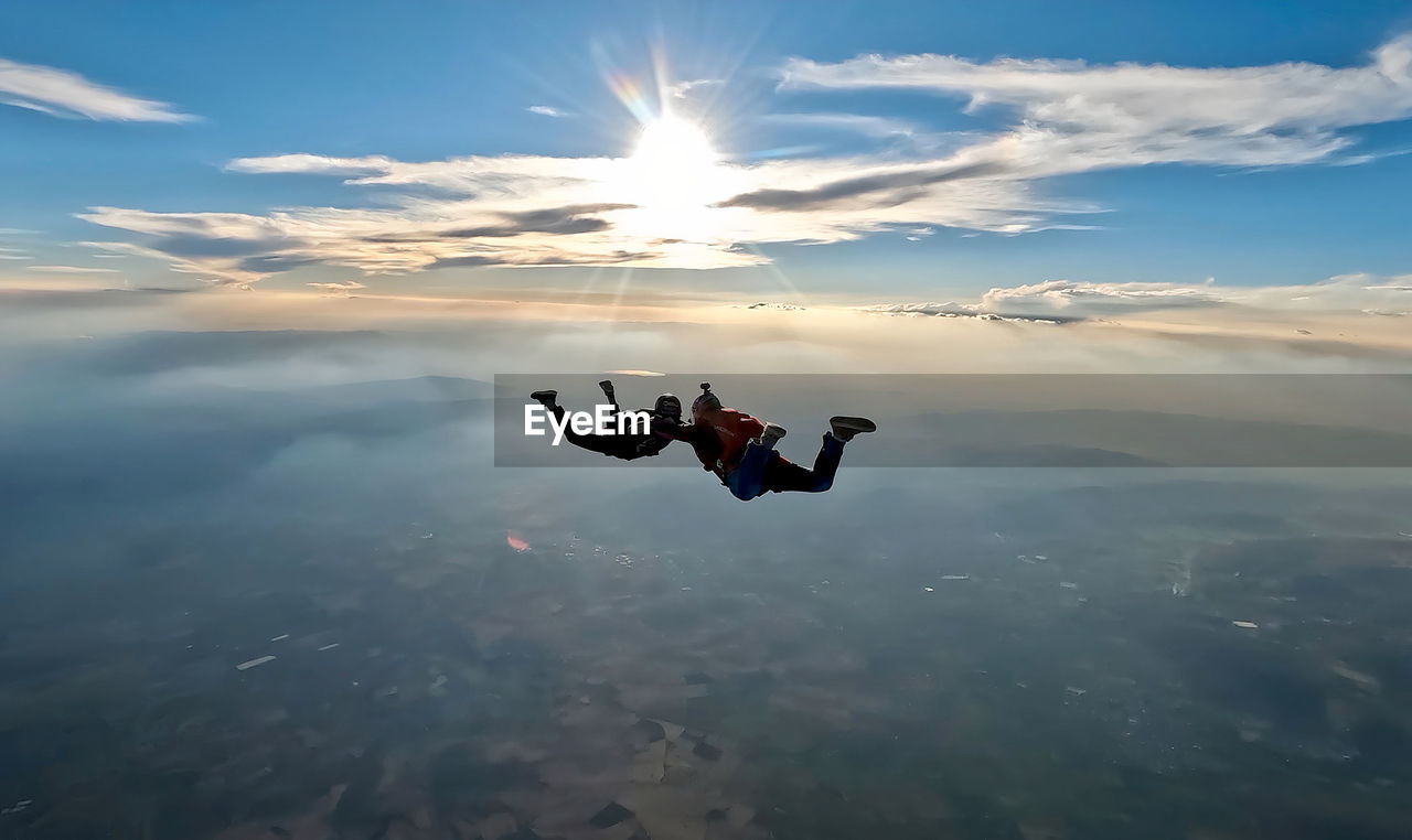 sky, parachuting, air sports, nature, mid-air, adventure, cloud, one person, windsports, sports, full length, flying, adult, skydiving, aerial view, extreme sports, tandem skydiving, motion, exhilaration, communication, joy, sunlight, leisure activity, environment, risk, parachute, men, jumping, day, outdoors, scenics - nature, warning sign, courage, landscape, vitality, beauty in nature, emotion, sign, activity, challenge, water, blue, mountain, skill, vacation, lifestyles, lens flare, positive emotion, tranquility, holiday