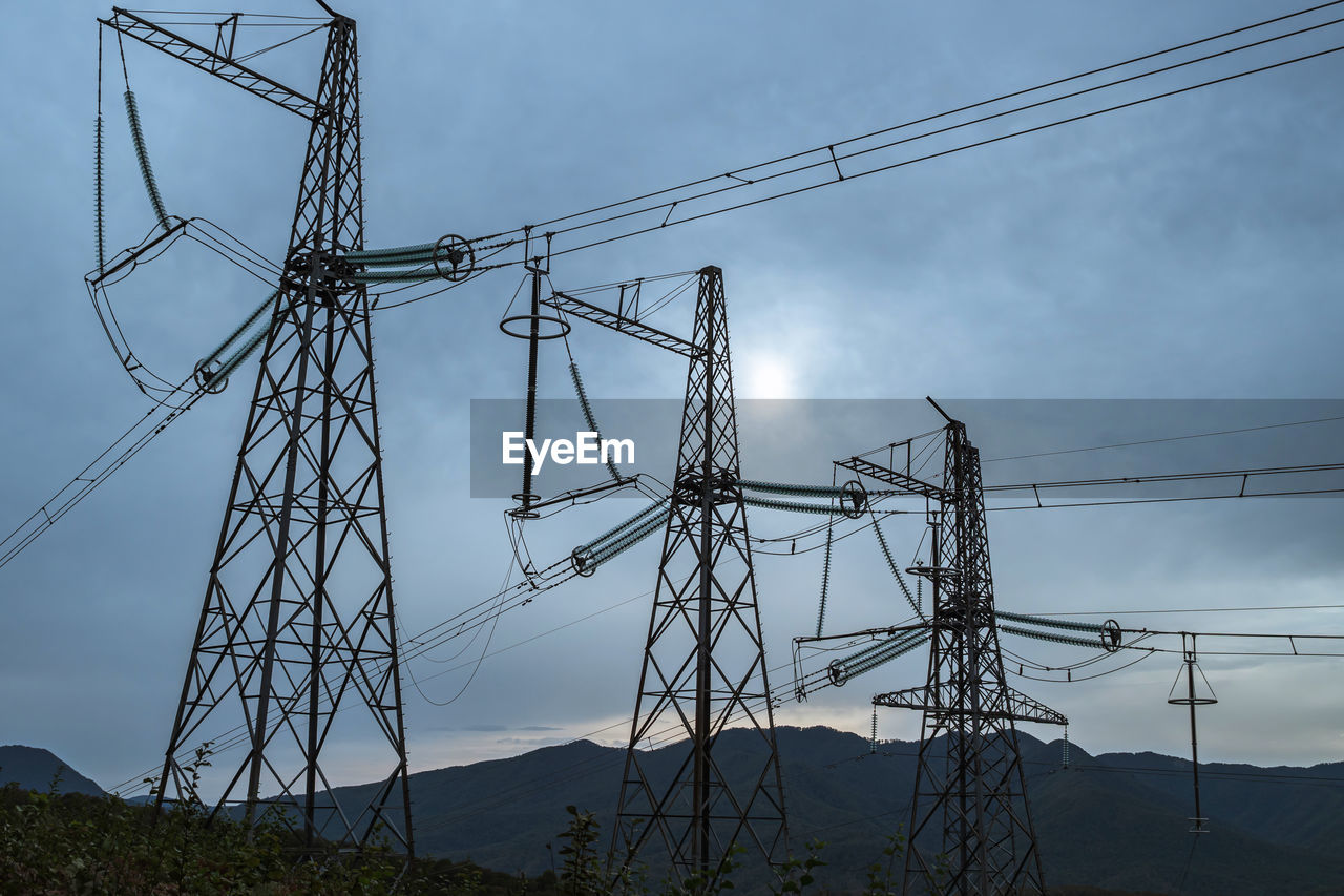 Transmission poles against the background of mountain hills and overcast sky