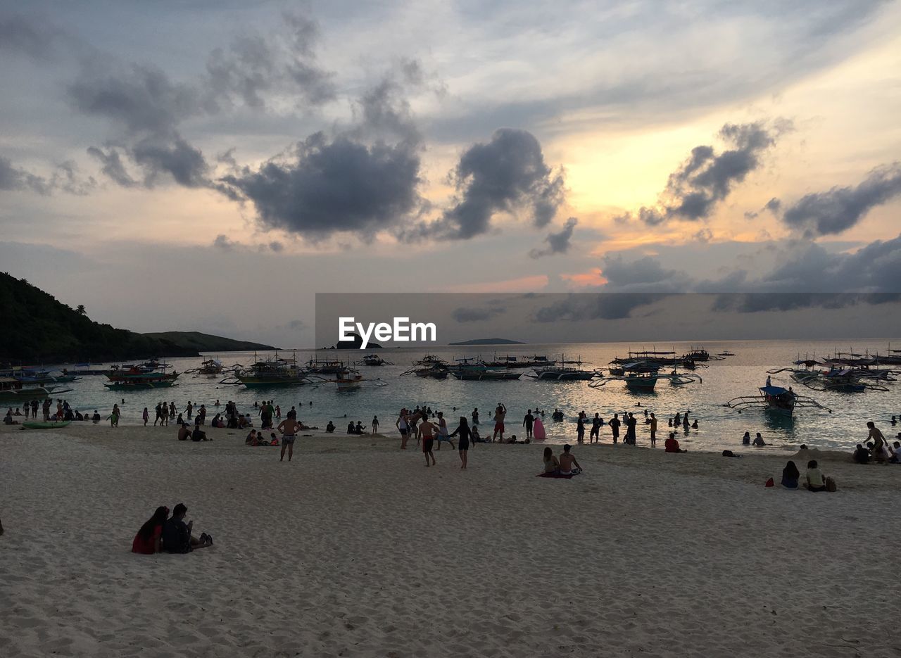 PEOPLE RELAXING AT BEACH DURING SUNSET