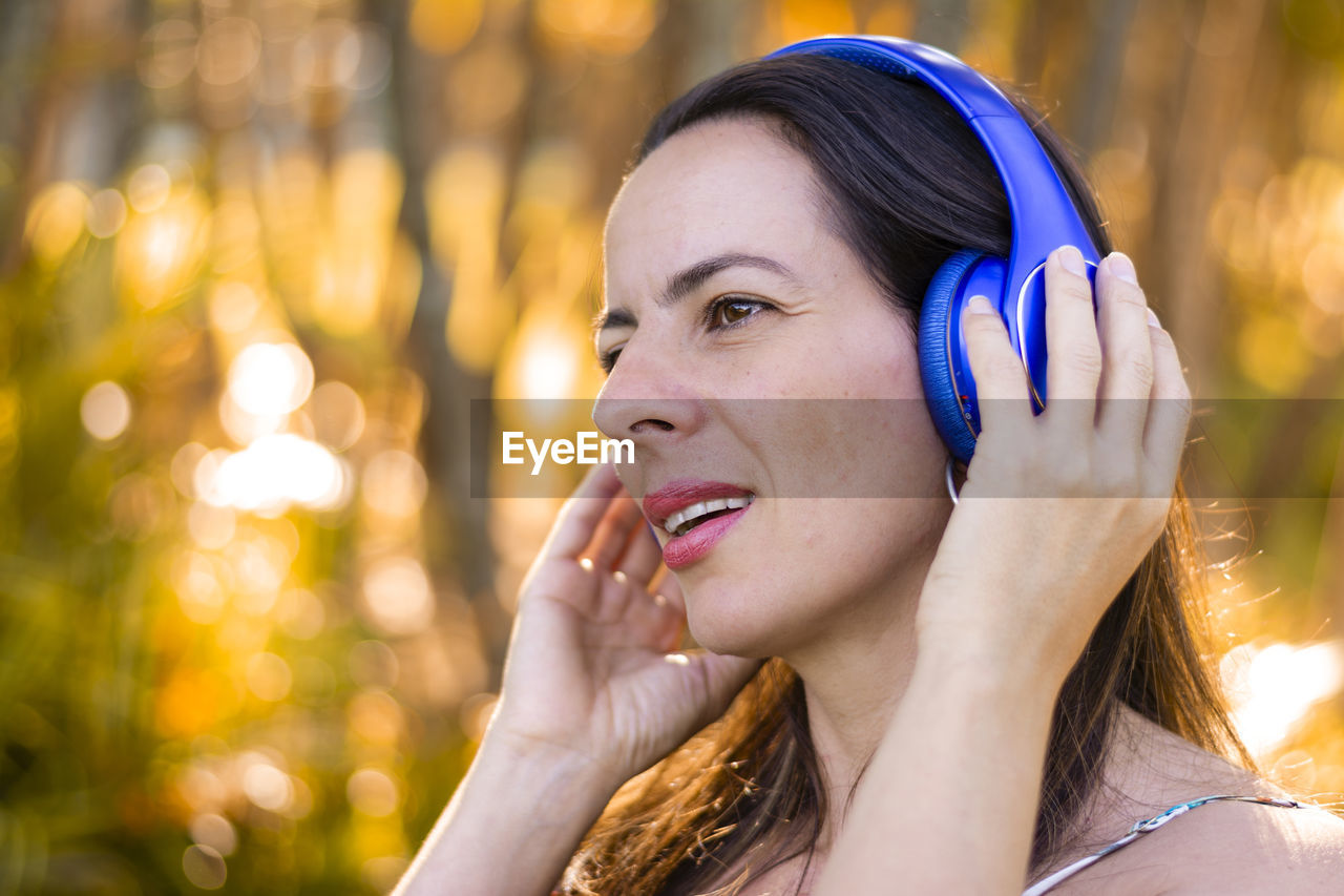 Close-up of mature woman listening to music through headphones against trees