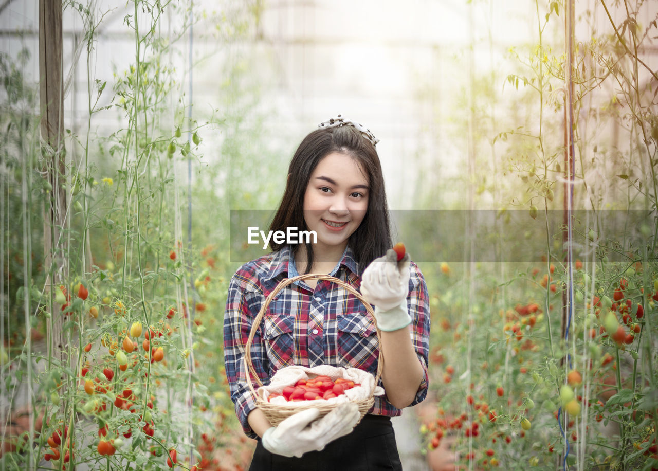 Portrait of smiling young woman holding strawberry at farm