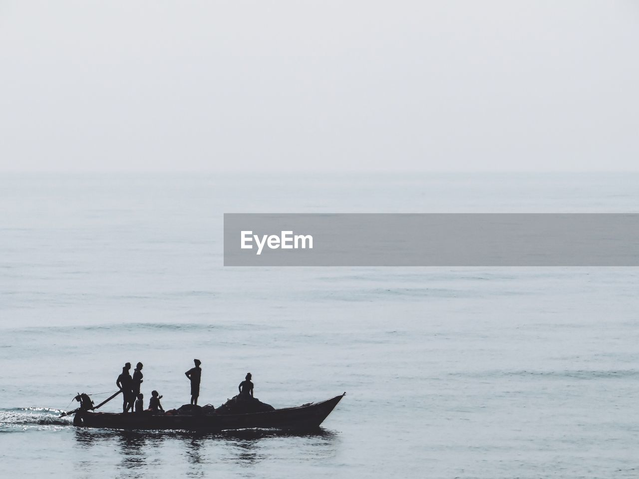 Silhouette people in boat on sea against sky