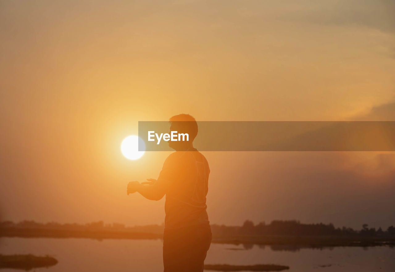 Silhouette man standing by lake against sky during sunset