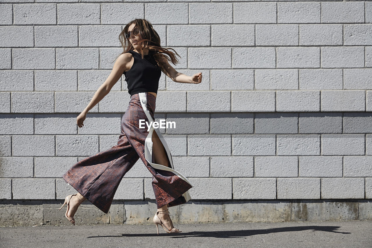 Fashionable young woman passing brick wall