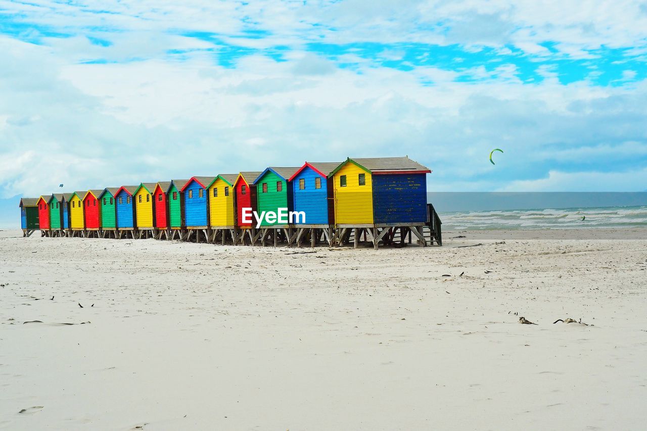 Multi colored huts on beach against cloudy sky