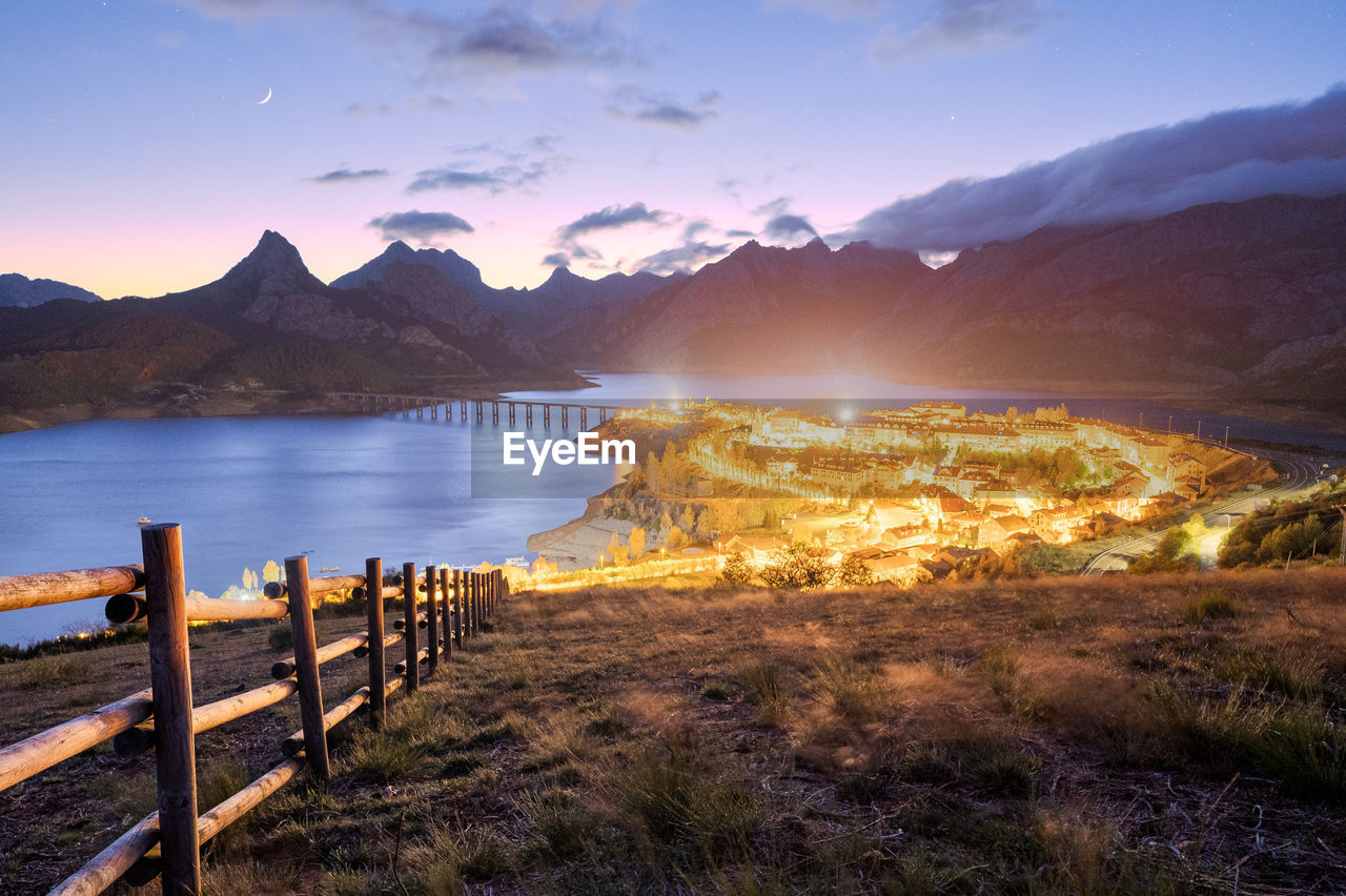 Breathtaking scenery of small town located near river surrounded by massive rocky mountains under scenic sunset sky in riano