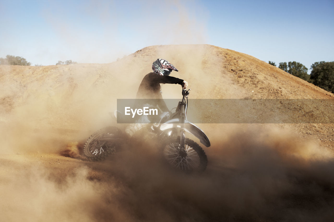 Man riding dirt bike on sand against sky