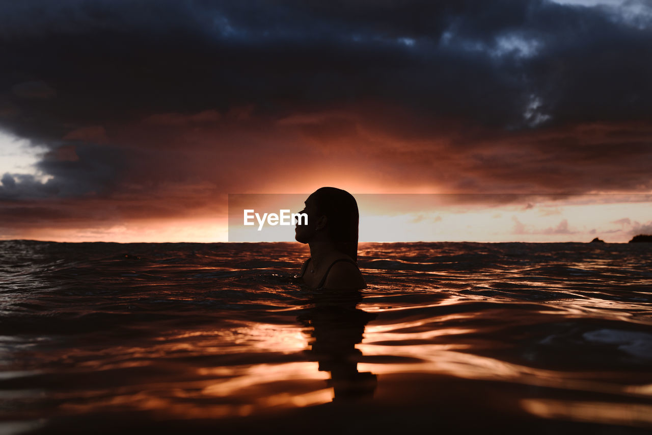 WOMAN STANDING AT BEACH DURING SUNSET