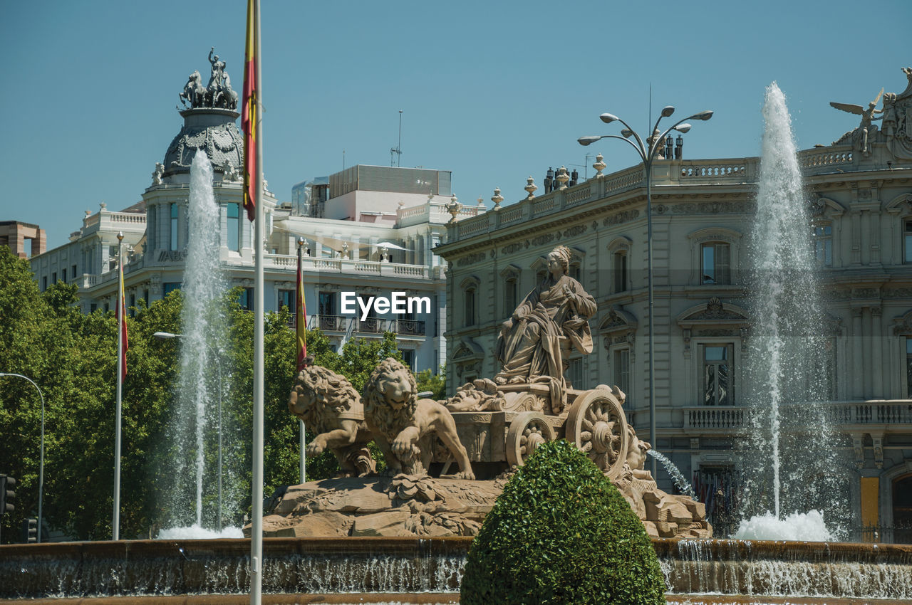 Charming cybele fountain with spanish flags and old buildings on the alcala street in madrid, spain.