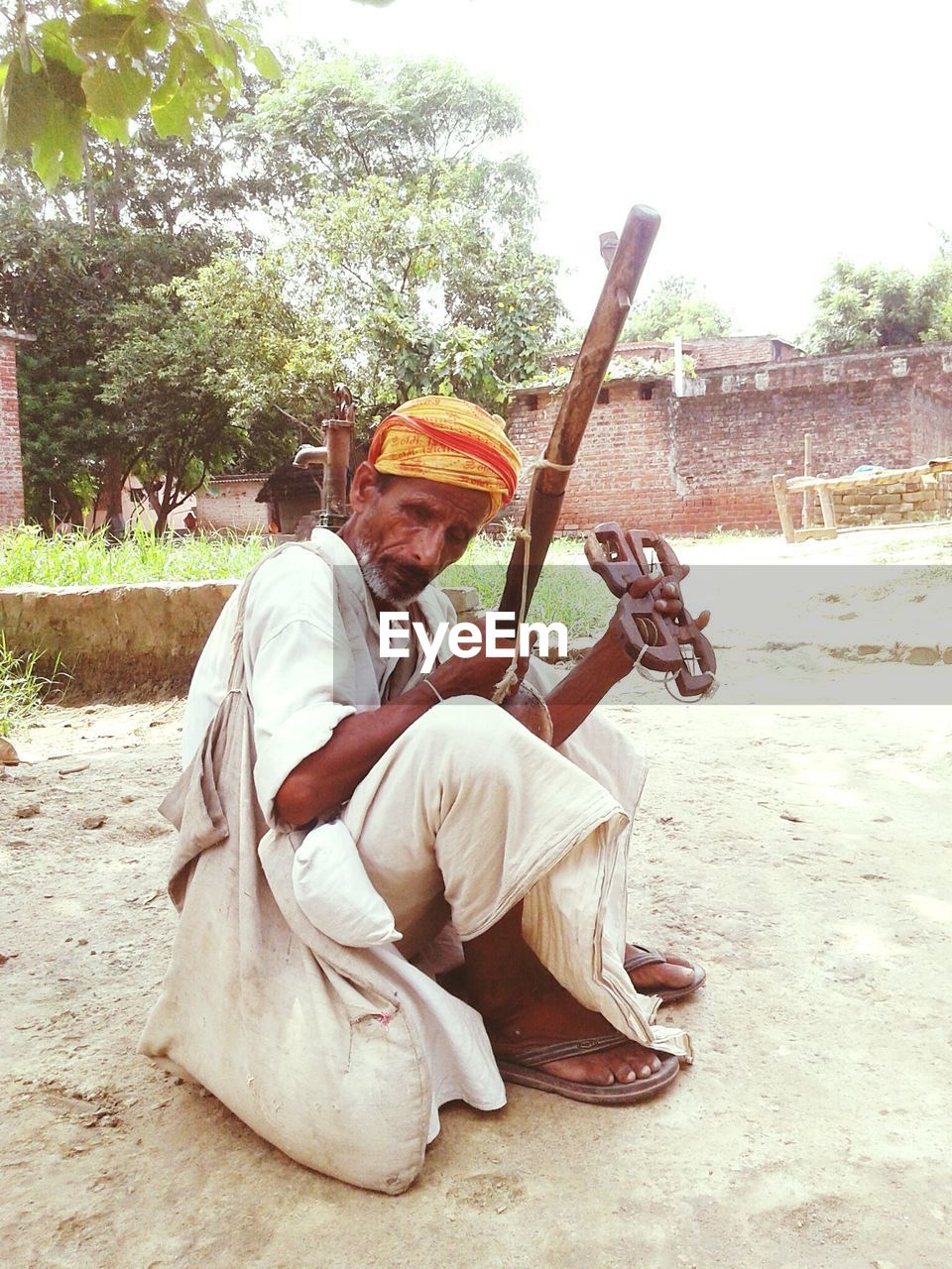 Street musician playing khartal while sitting on field
