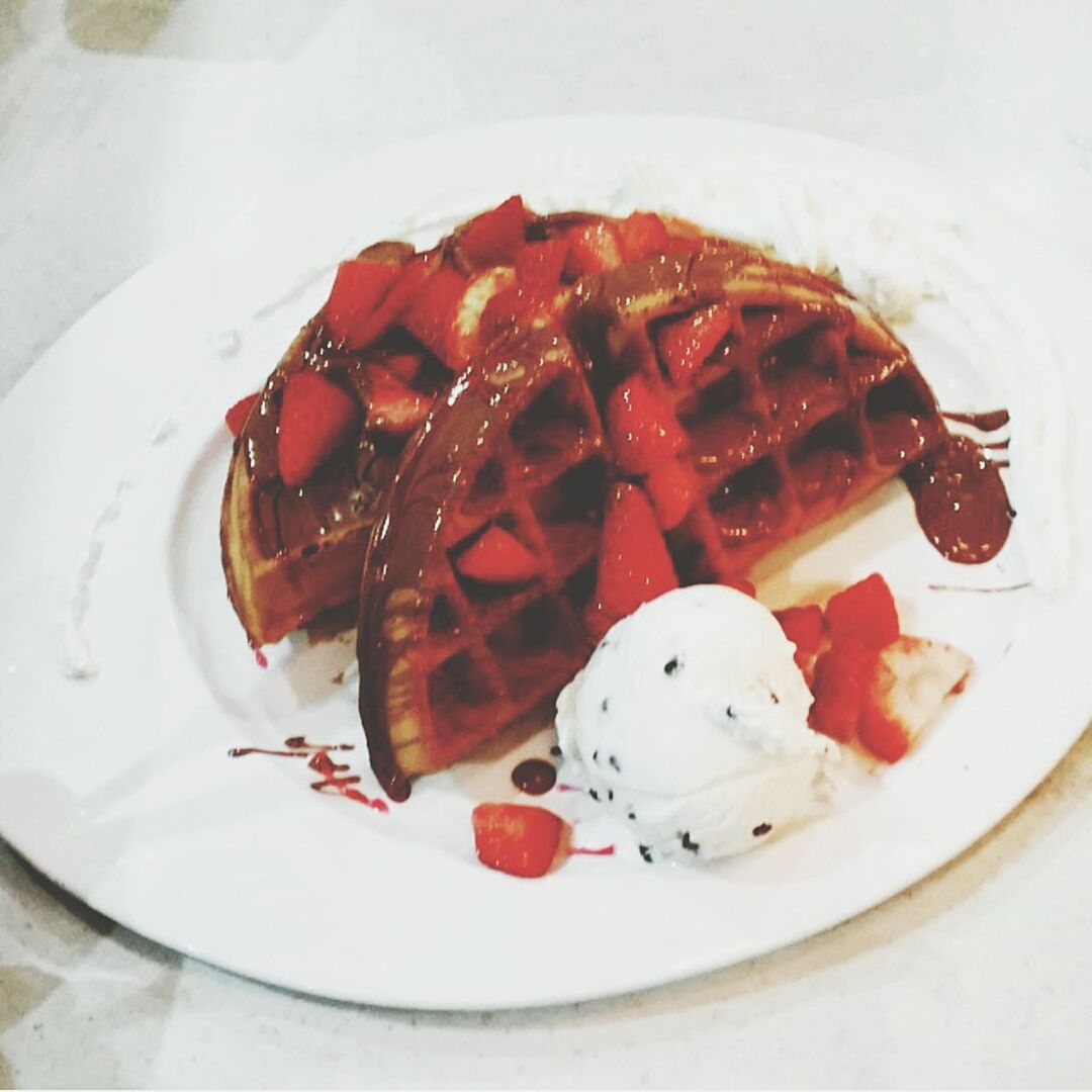 High angle view of waffle with strawberry syrup and ice cream in plate