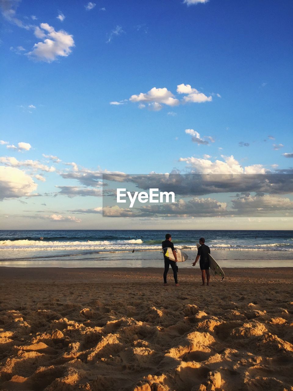 REAR VIEW OF FRIENDS ON BEACH AGAINST SKY